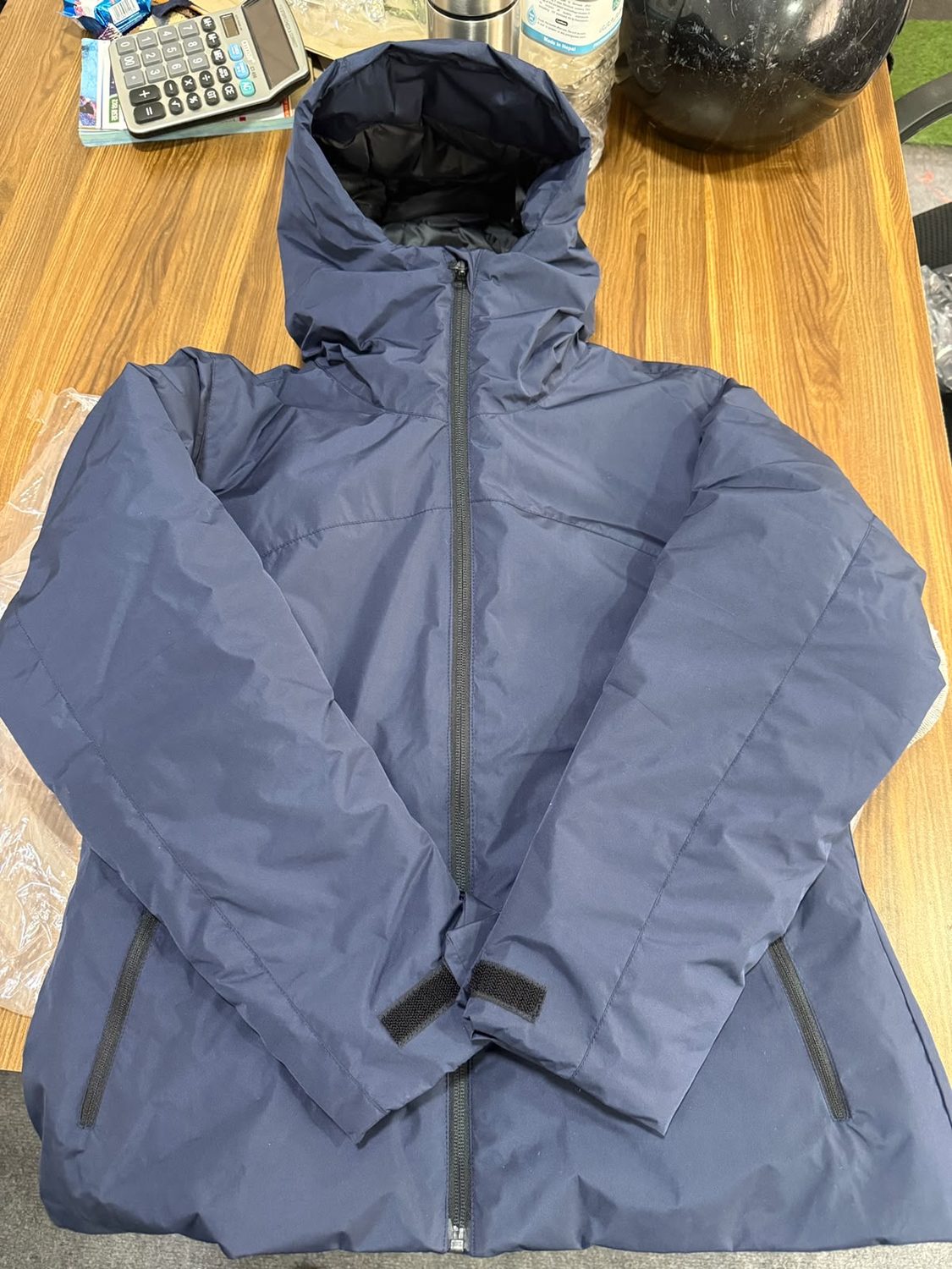 A navy hooded jacket laid closed on a wooden table, with hook and loop tabs at both cuffs and zipped side pockets