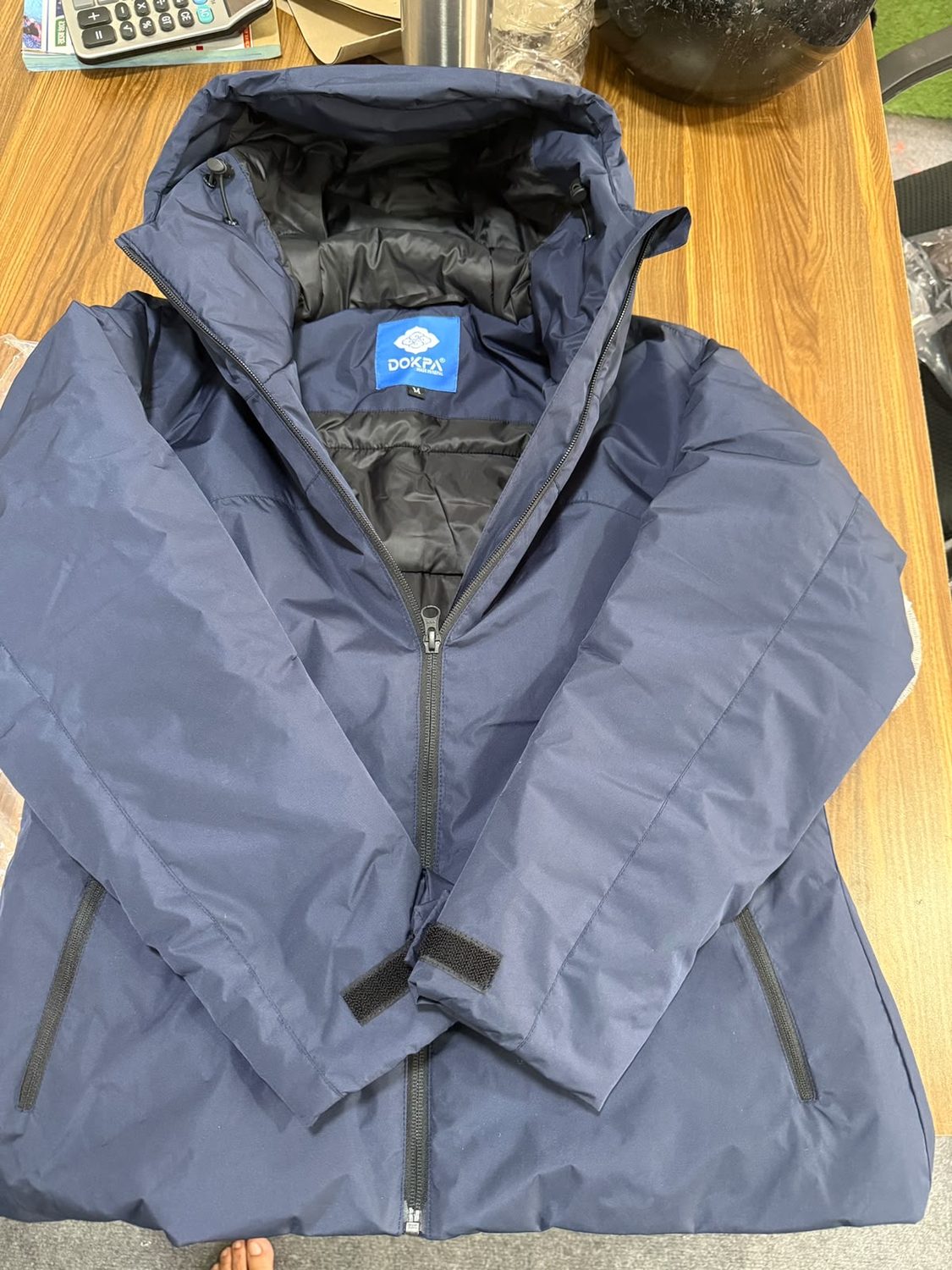 A navy jacket opened at the neck showing the blue Dokpa woven label and a small white M tag at the inside collar