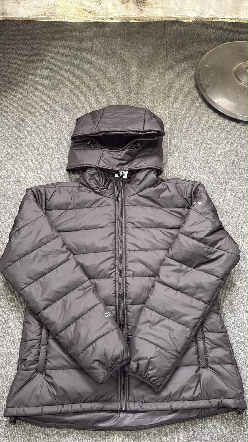 A charcoal quilted jacket on grey carpet with its hood laid clear above the collar and quilting in horizontal channels