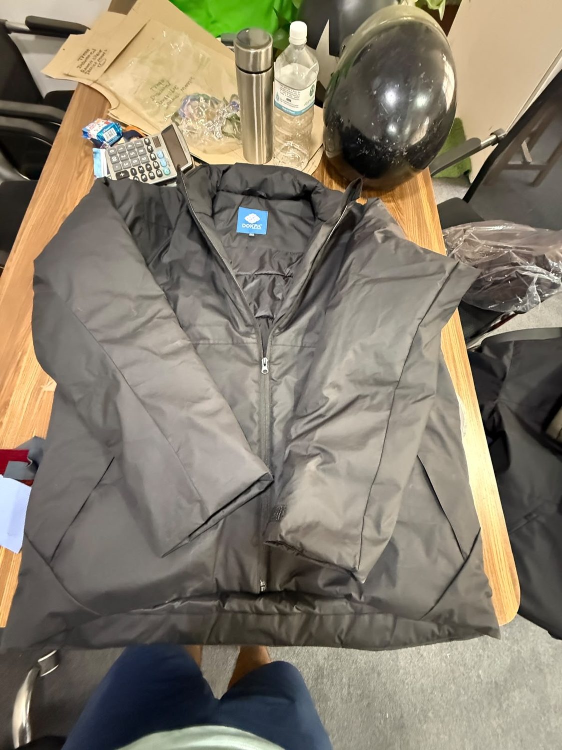 A dark grey jacket opened wide on a wooden workroom desk showing a small blue label at the inside collar